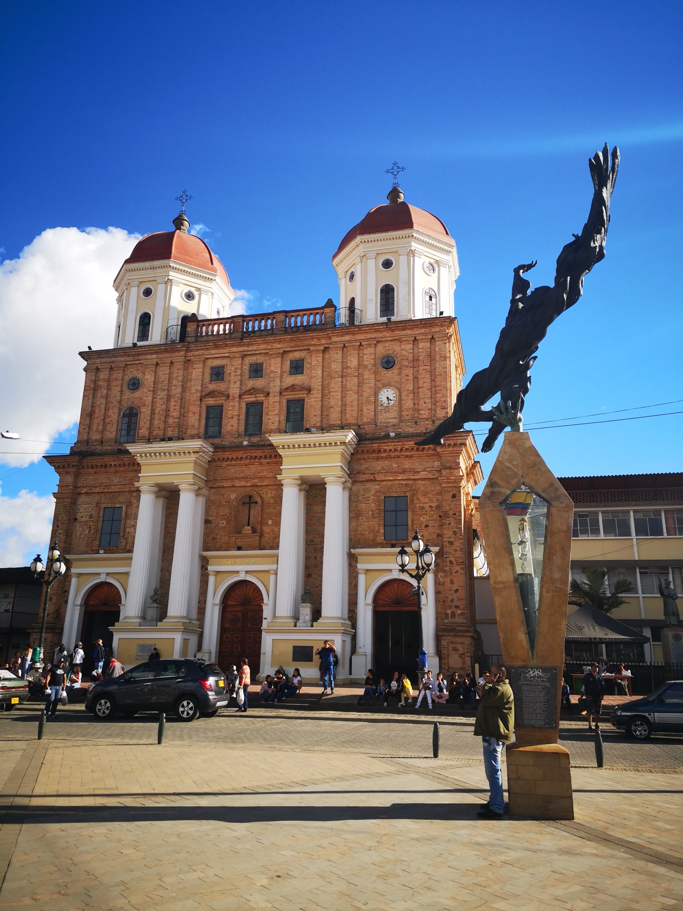 Fachada de la catedral de Santa Rosa de Osos bajo un cielo azul, con sus cúpulas rojas y columnas blancas.